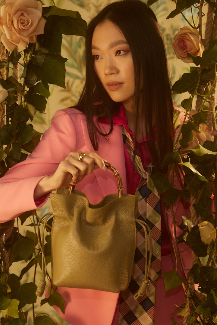 Woman in pink blazer holding olive green handbag surrounded by roses