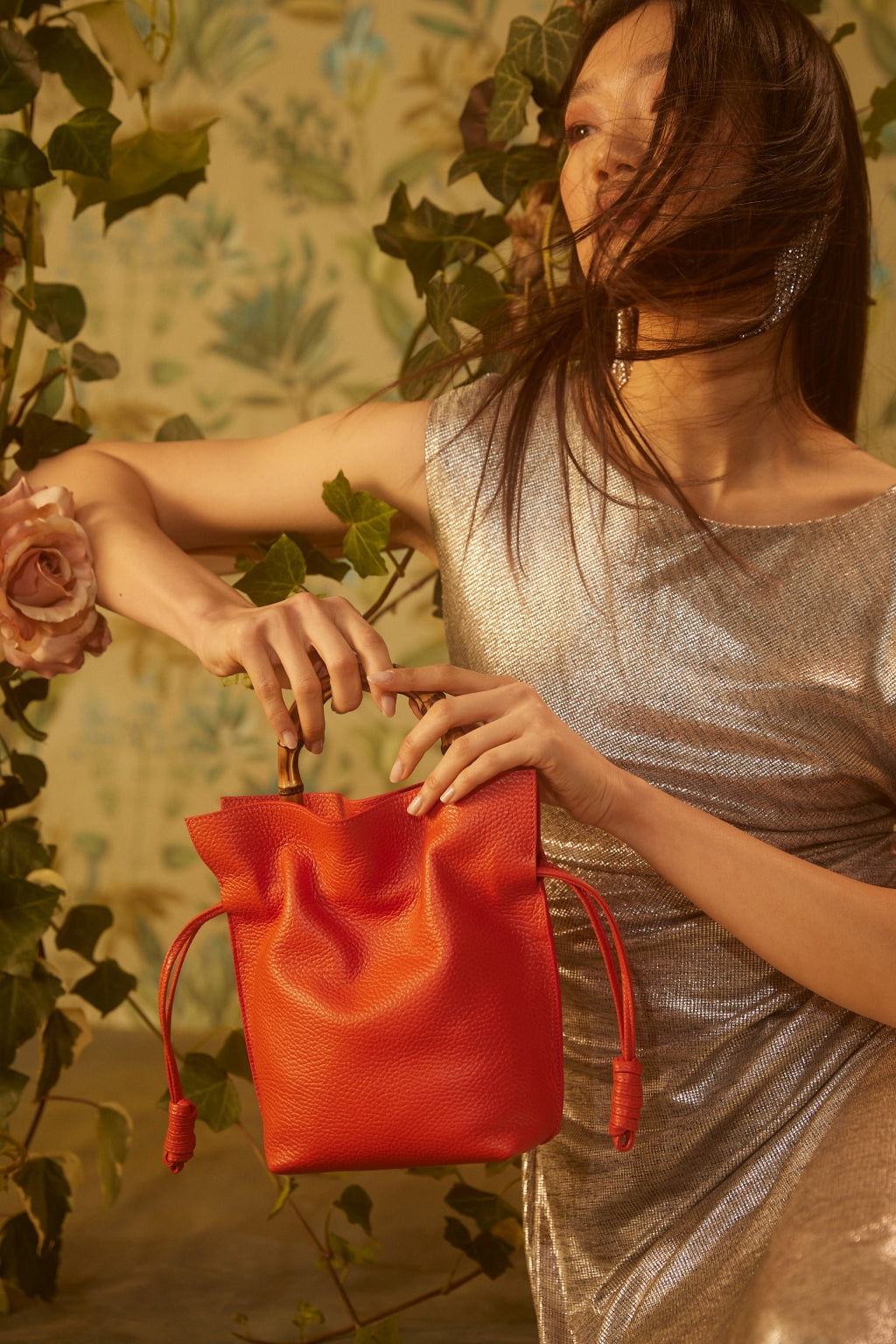 Woman in silver dress holding red handbag with floral background