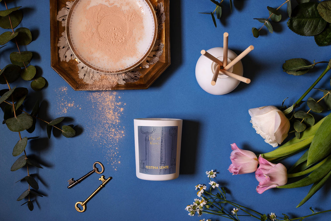 Decorative candle, flowers, eucalyptus leaves, and vintage keys arranged on blue background