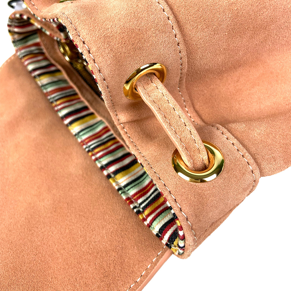 Close-up of a blush suede handbag with gold eyelets and a colorful striped interior lining