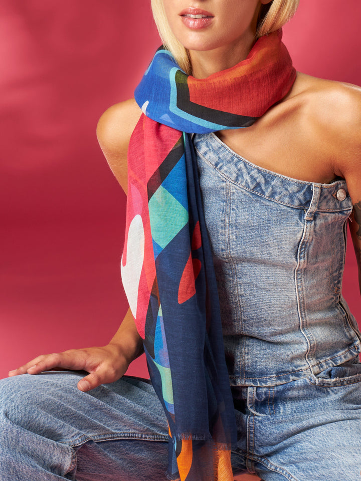Woman wearing colorful geometric scarf and denim overalls against pink background