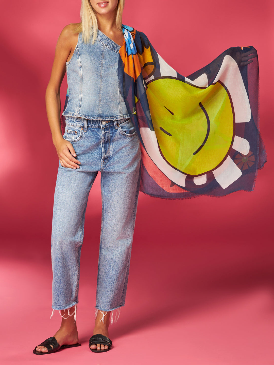 Blonde woman in denim outfit with colorful scarf holds corner of smiling face illustration on a pink background