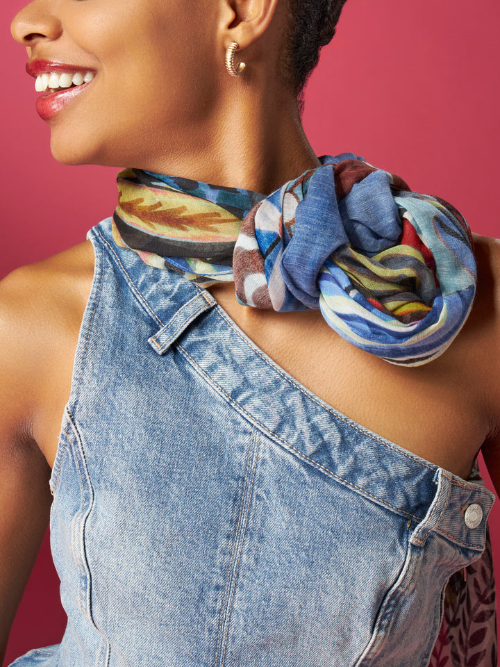 Woman wearing a colorful scarf and denim dress against a pink background