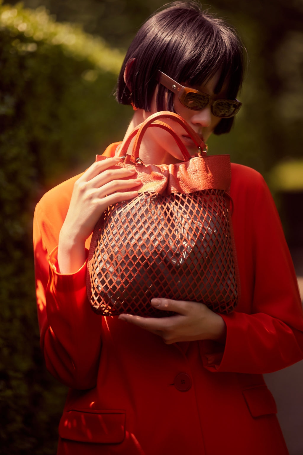 Woman in red coat holding a stylish woven handbag outdoors