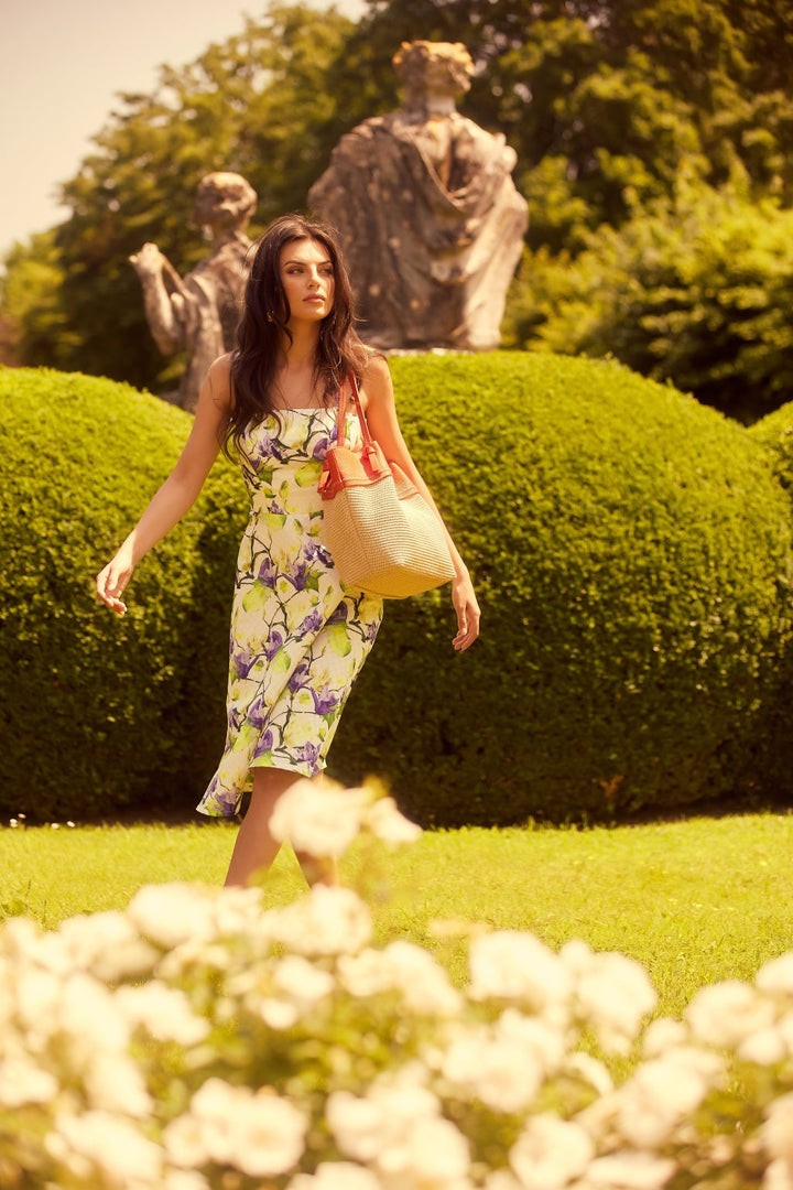 Woman in floral dress walking in a garden with statues and trimmed hedges