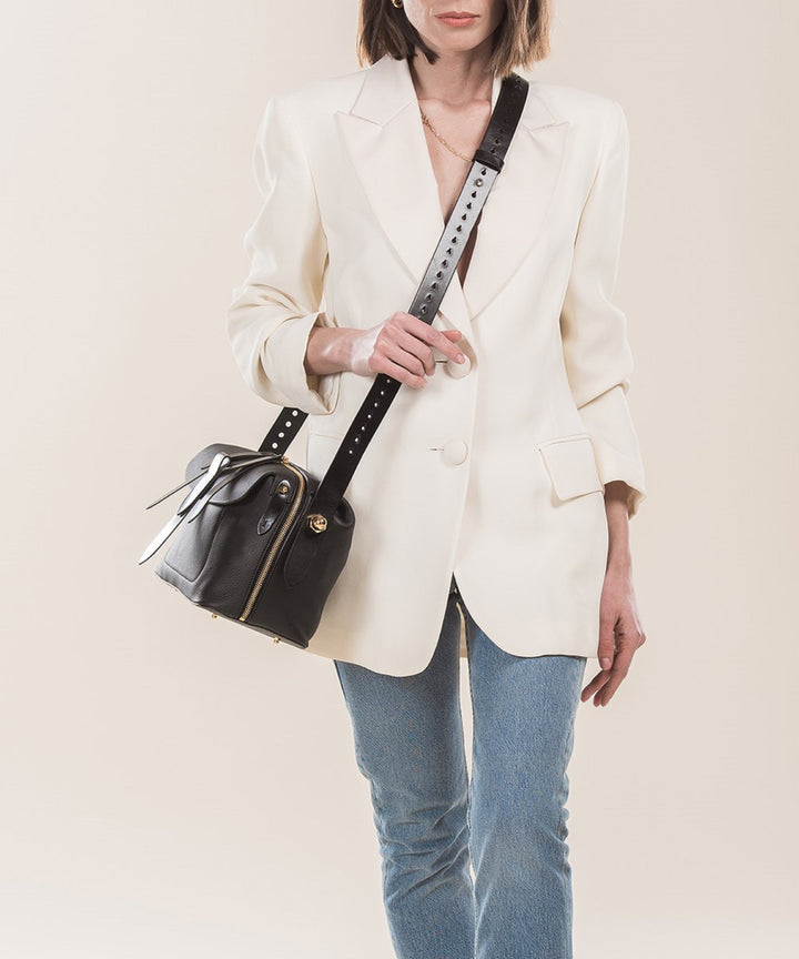 Woman in white blazer and blue jeans carrying black leather shoulder bag