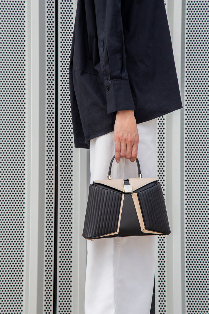 Person holding a stylish black and beige handbag with geometric patterns against a modern metallic background