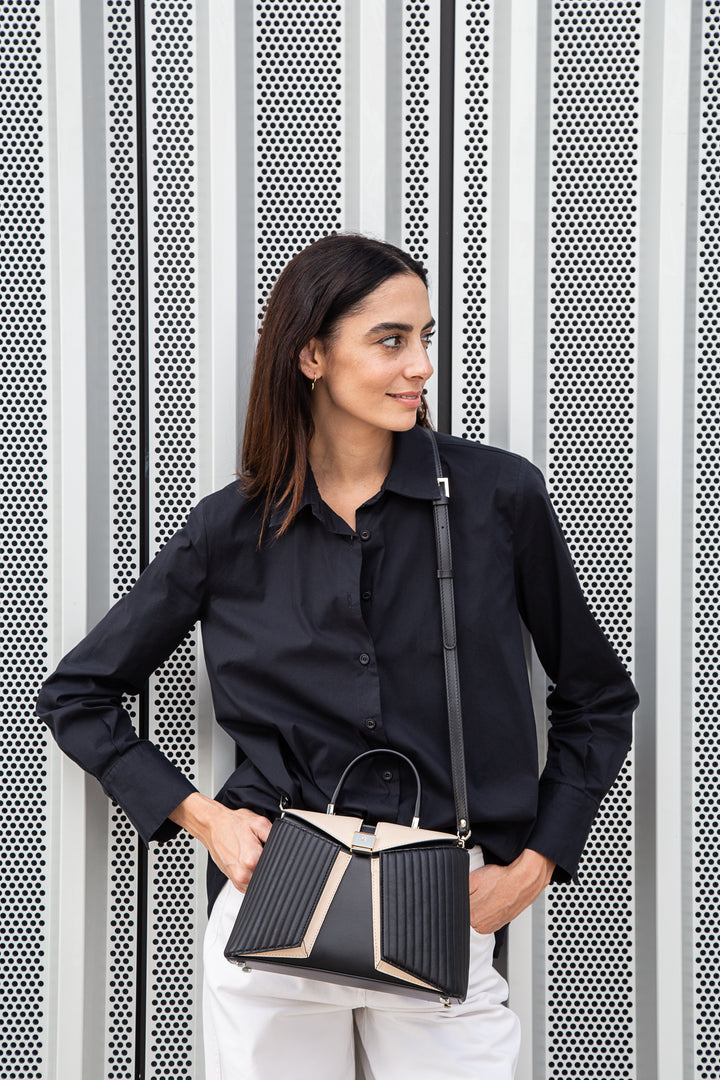 Woman in black shirt holding a stylish handbag against a modern metallic background