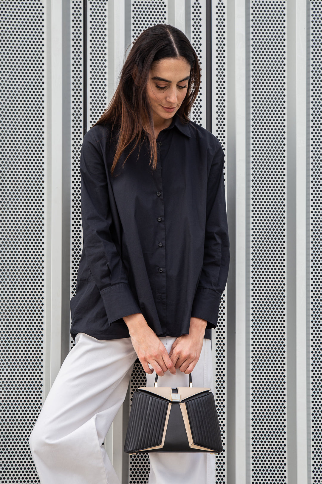 Woman in black shirt and white pants holding a stylish black handbag