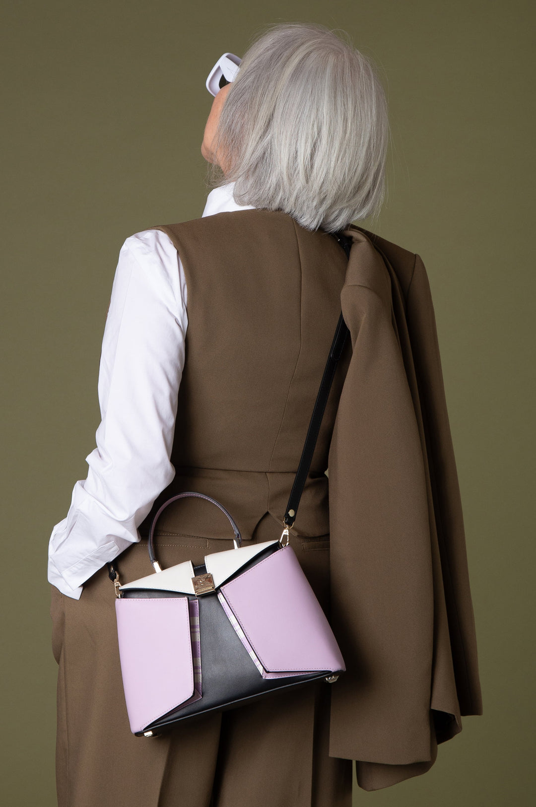 Senior woman with gray hair in stylish brown outfit and white shirt, carrying a fashionable pink and black handbag