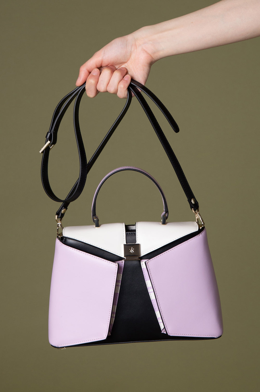 Hand holding stylish pink and black handbag against olive background