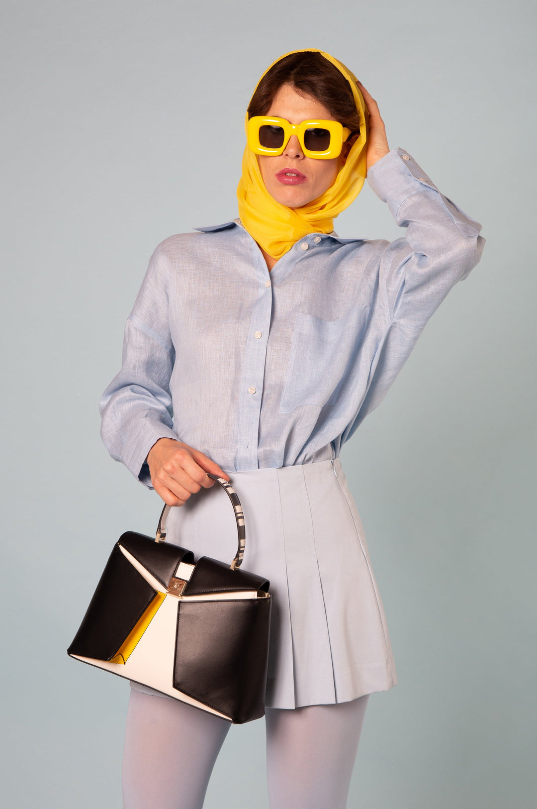 Woman in stylish clothing with yellow headscarf and sunglasses holding a black and white handbag