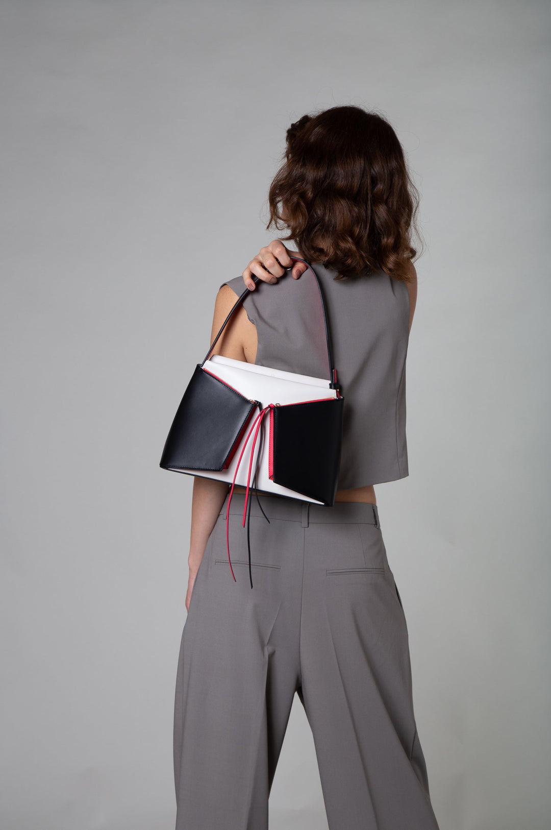 Woman in grey outfit showcasing a stylish black and white handbag with red accents