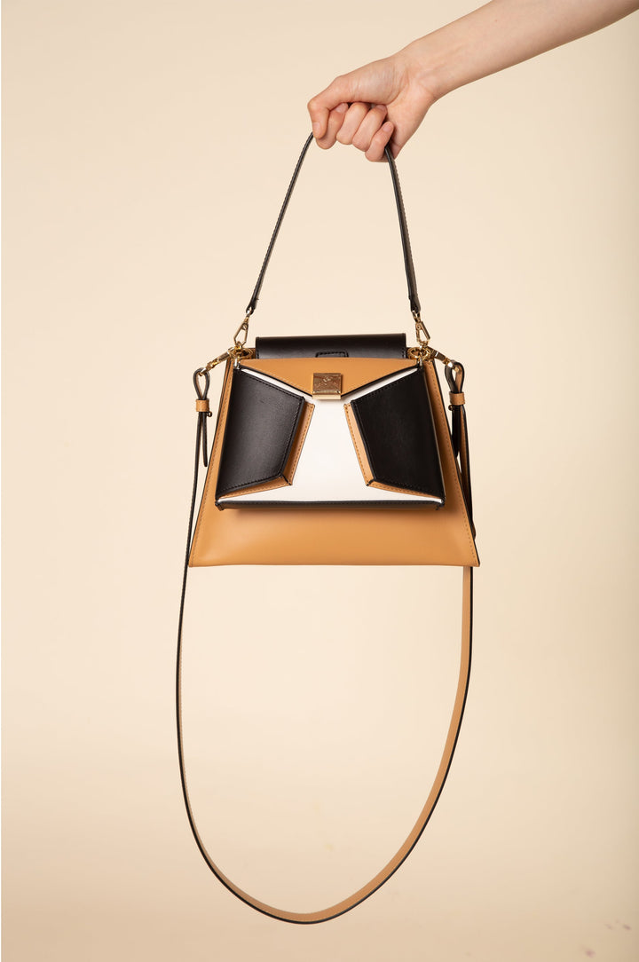 Hand holding a stylish beige and black designer handbag with long shoulder strap