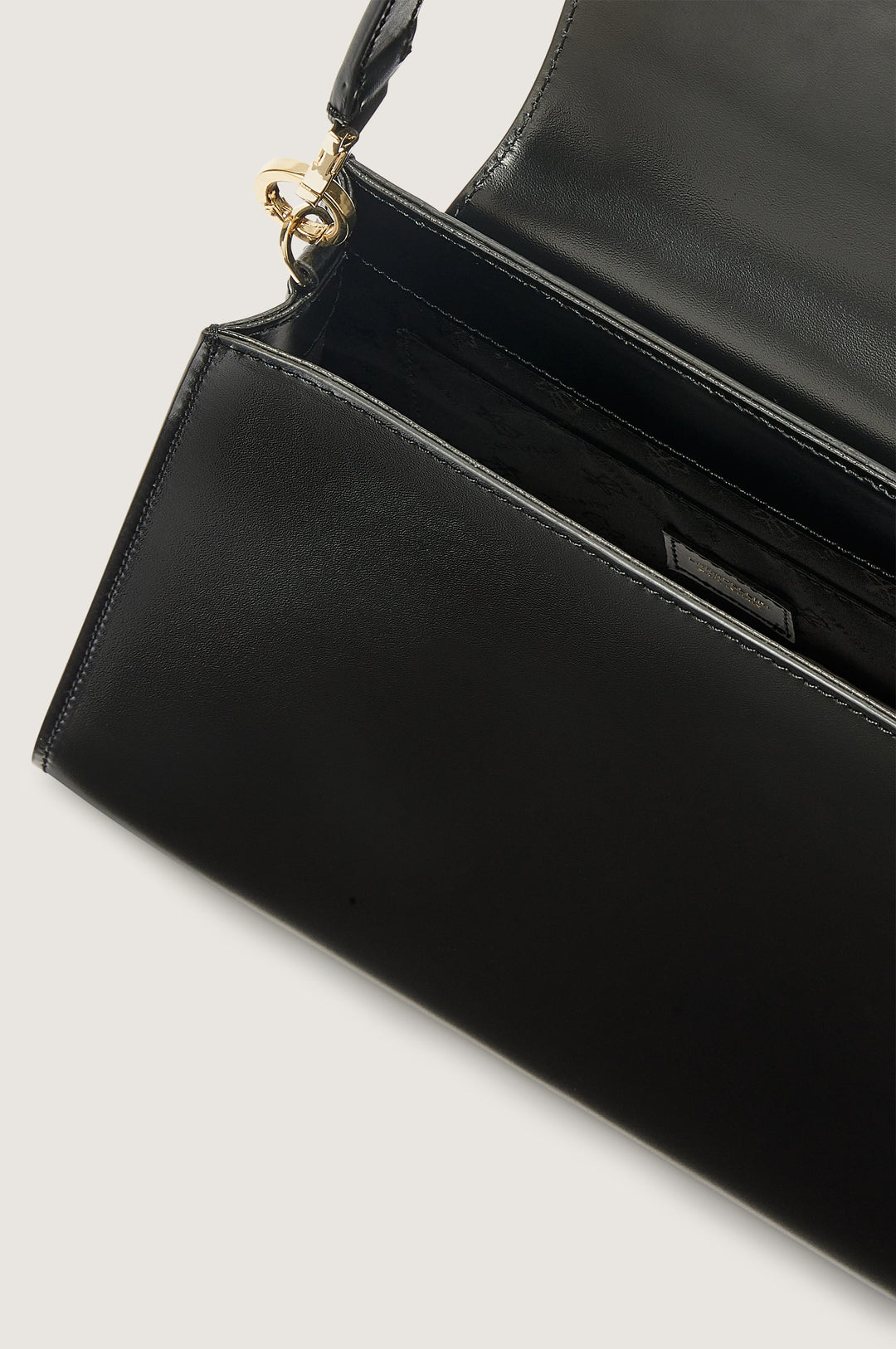 Black leather handbag with gold clasp and open flap showing inner compartment