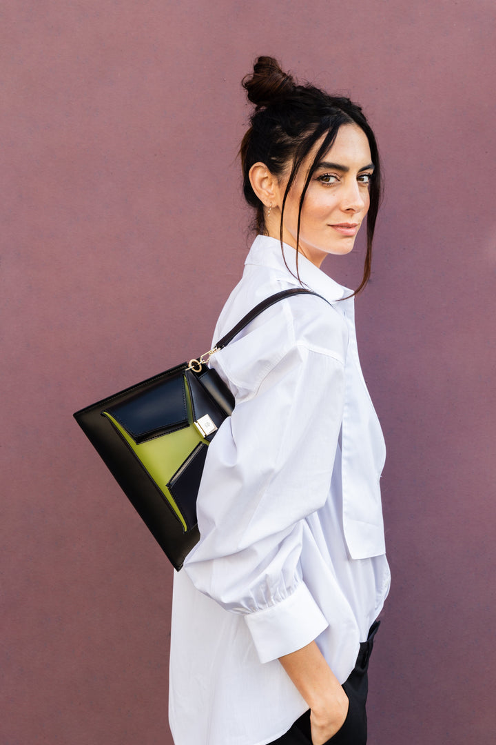 Woman wearing a white blouse holding a stylish triangular handbag against a purple background