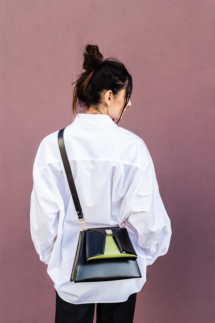 Woman in white shirt with stylish black handbag against pink wall