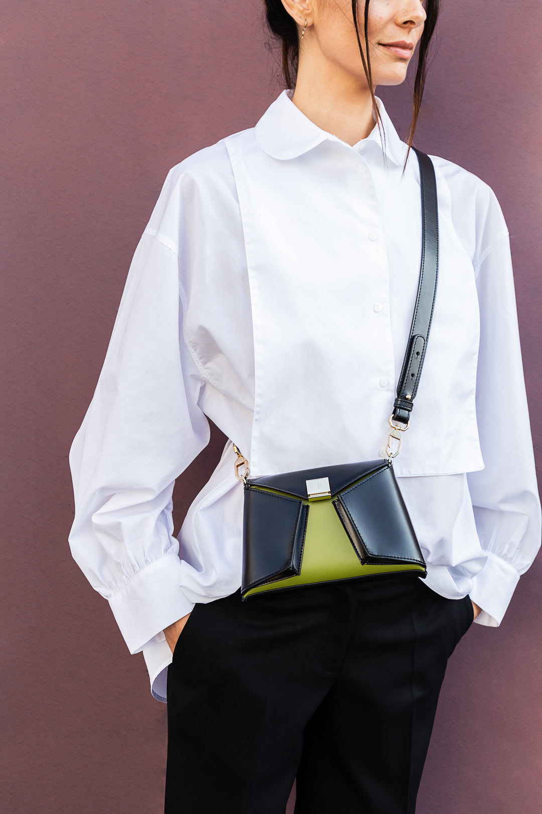 Woman wearing white shirt with black and green crossbody bag against purple background