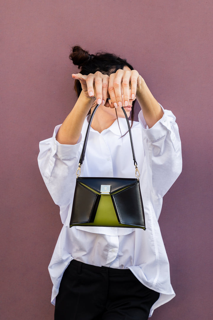 Woman holding small stylish handbag against a purple wall