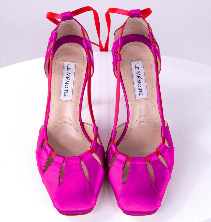 Bright pink high-heeled shoes with red ankle straps on a white background