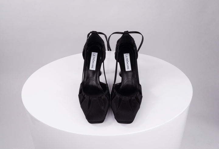 Elegant black high-heeled shoes on white pedestal