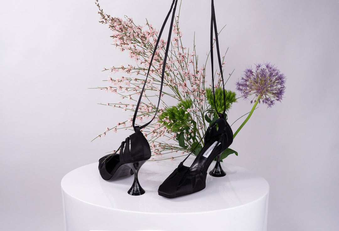 Black high-heeled shoes with ribbons displayed against a floral background