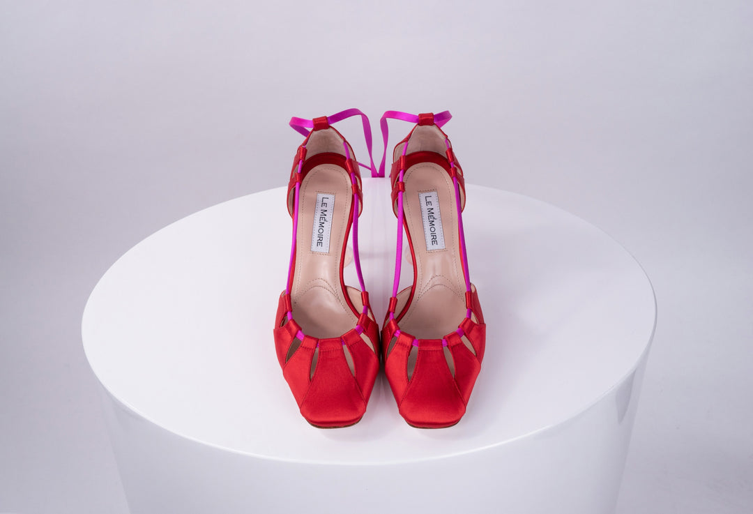 Red high-heeled shoes with pink straps displayed on a white surface