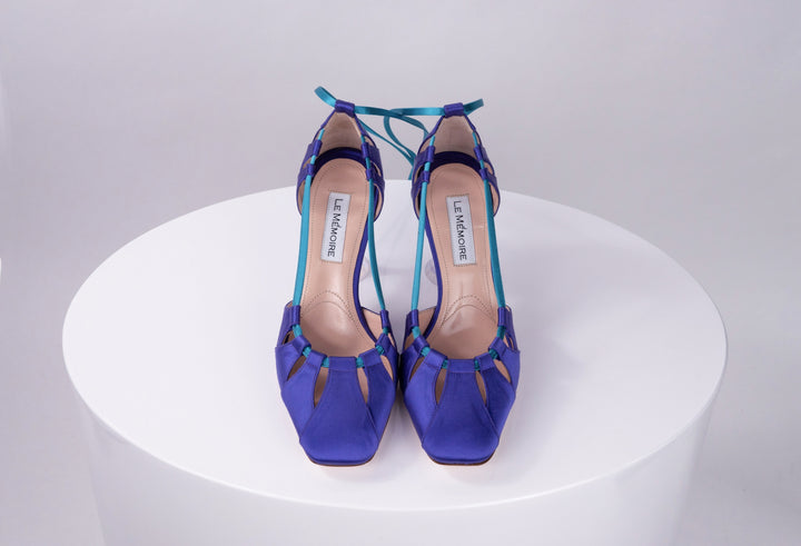Blue high-heeled sandals with strappy design on white pedestal