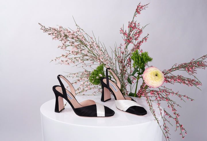 Black and white slingback heels displayed with pink and white flowers on a white platform