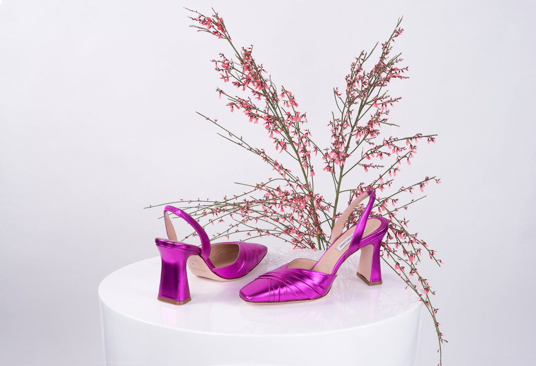 Bright pink high-heeled shoes with elegant design on white platform table next to delicate pink flowers