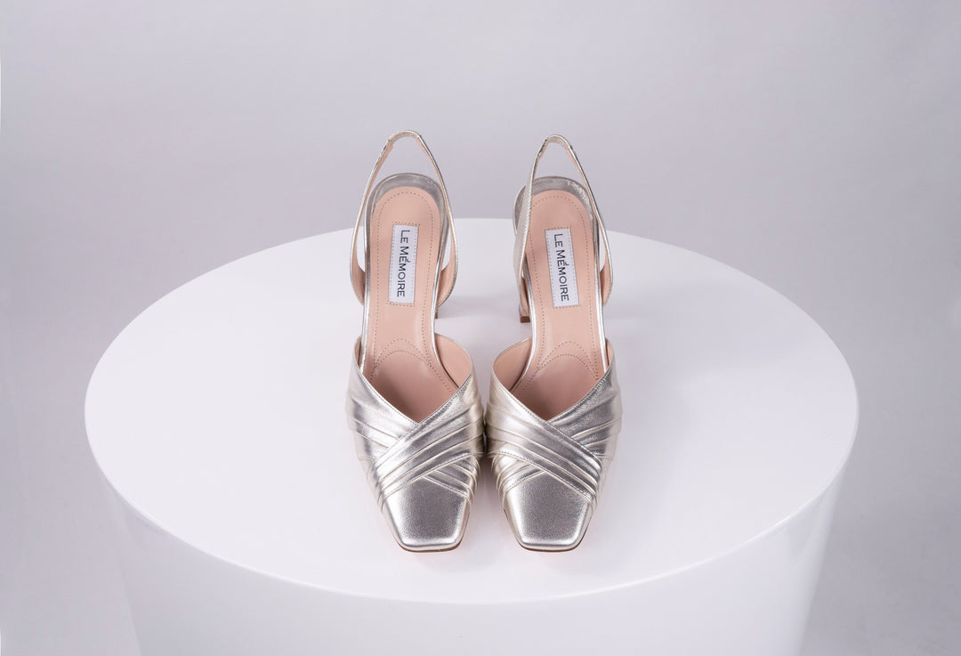 Silver high-heeled shoes with crisscross straps displayed on a white surface