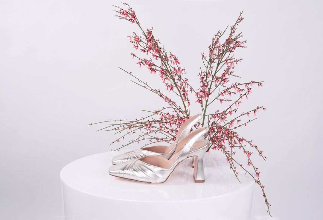 Silver high-heeled shoes with pink flowers on a white pedestal