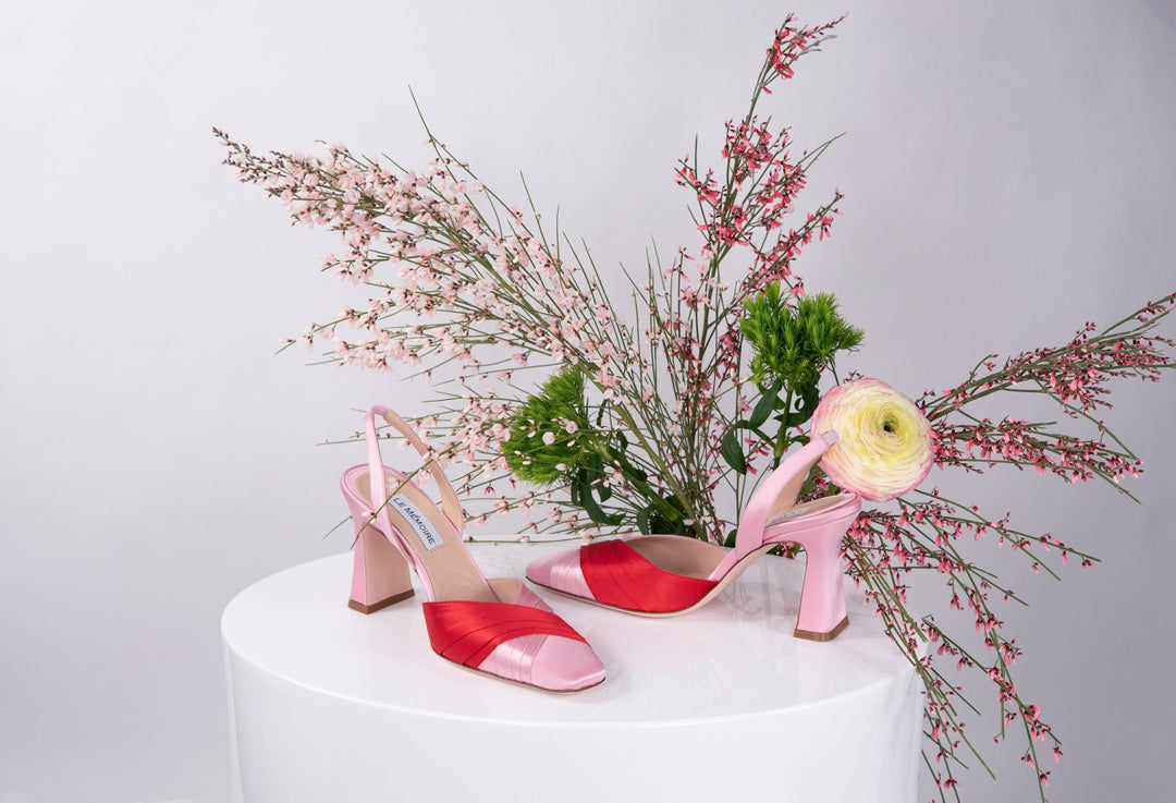 Pink and red high heels displayed on white pedestal with floral arrangement in background