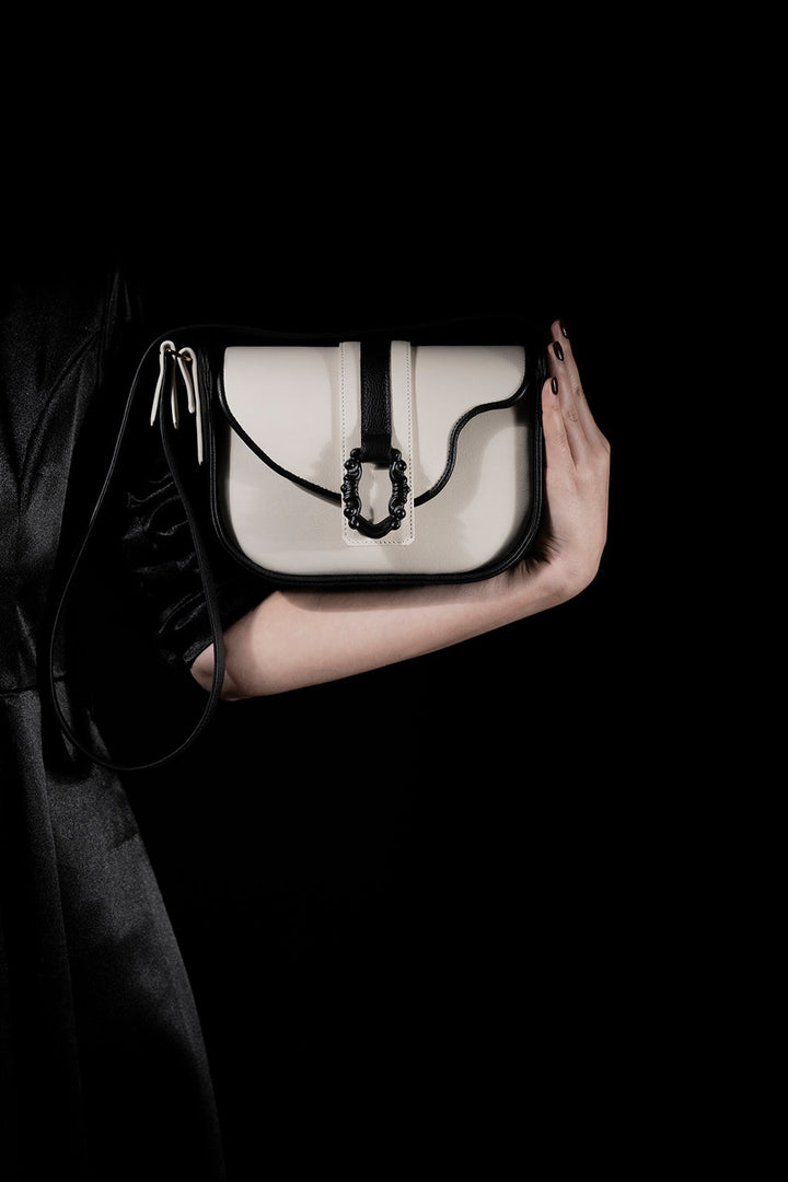 Person holding a stylish black and white handbag against a dark background