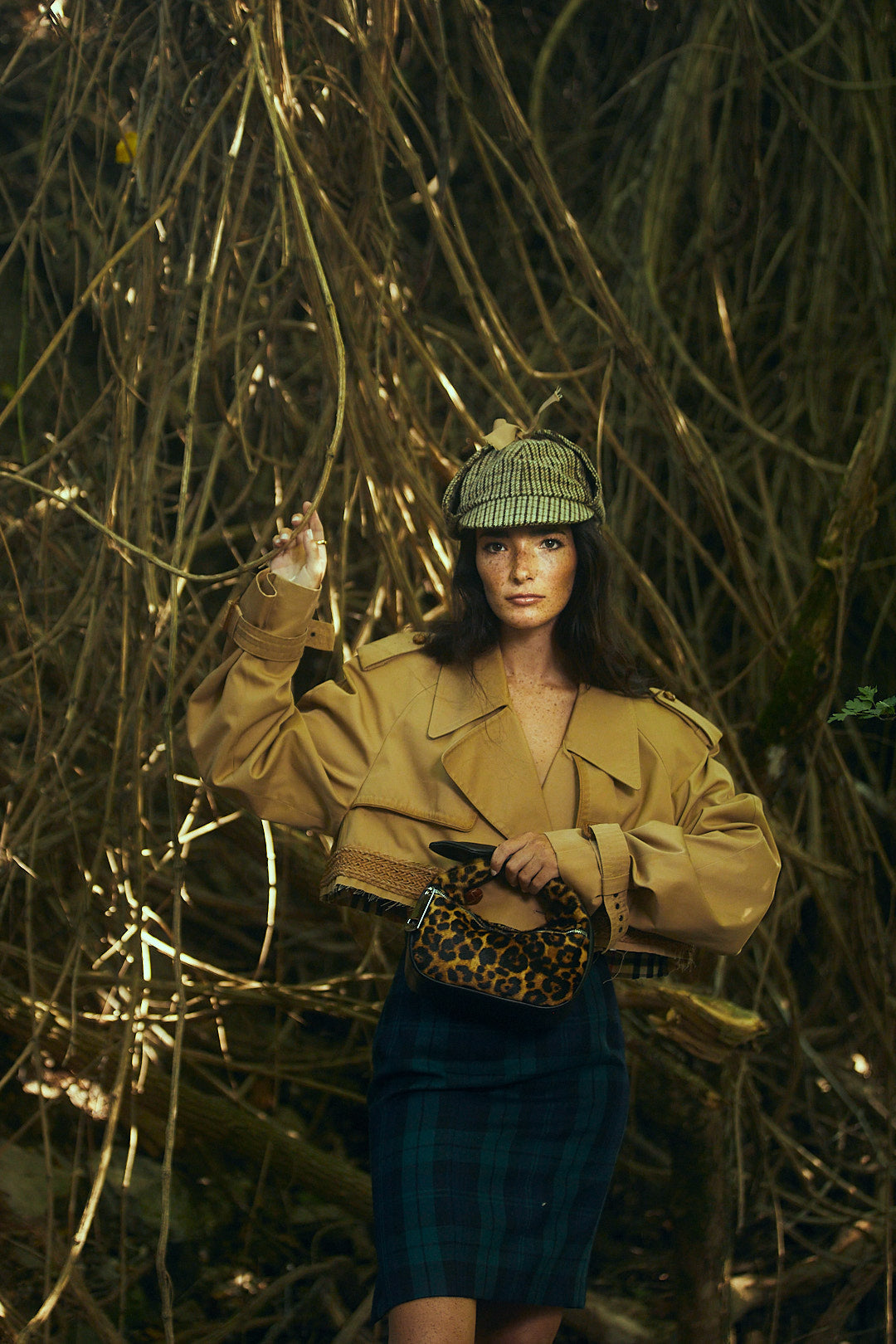 Woman wearing fashionable autumn outfit with jacket, plaid skirt, and checkered hat in forest setting