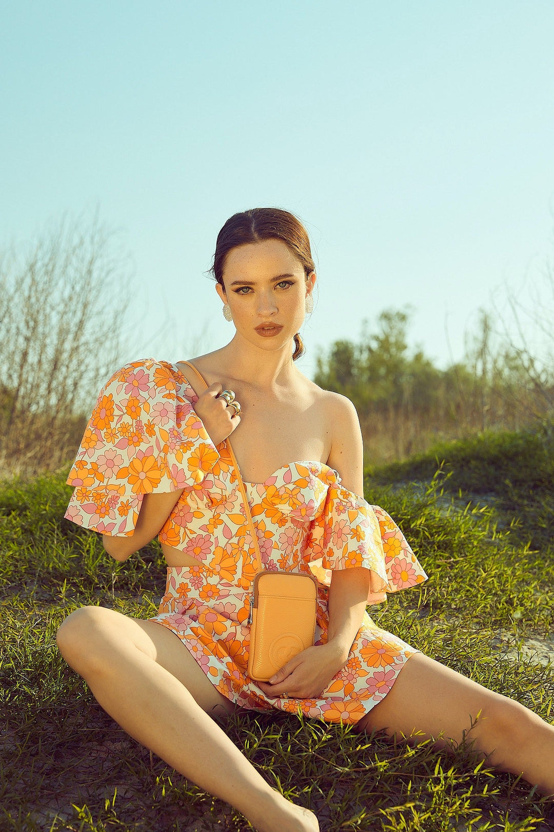 Woman wearing floral off-shoulder dress sitting outdoors in grassy field