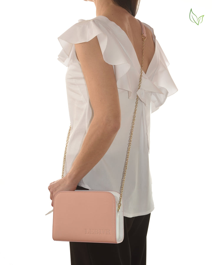 Woman wearing a white ruffle sleeve top holding a pink and white handbag with gold chain strap