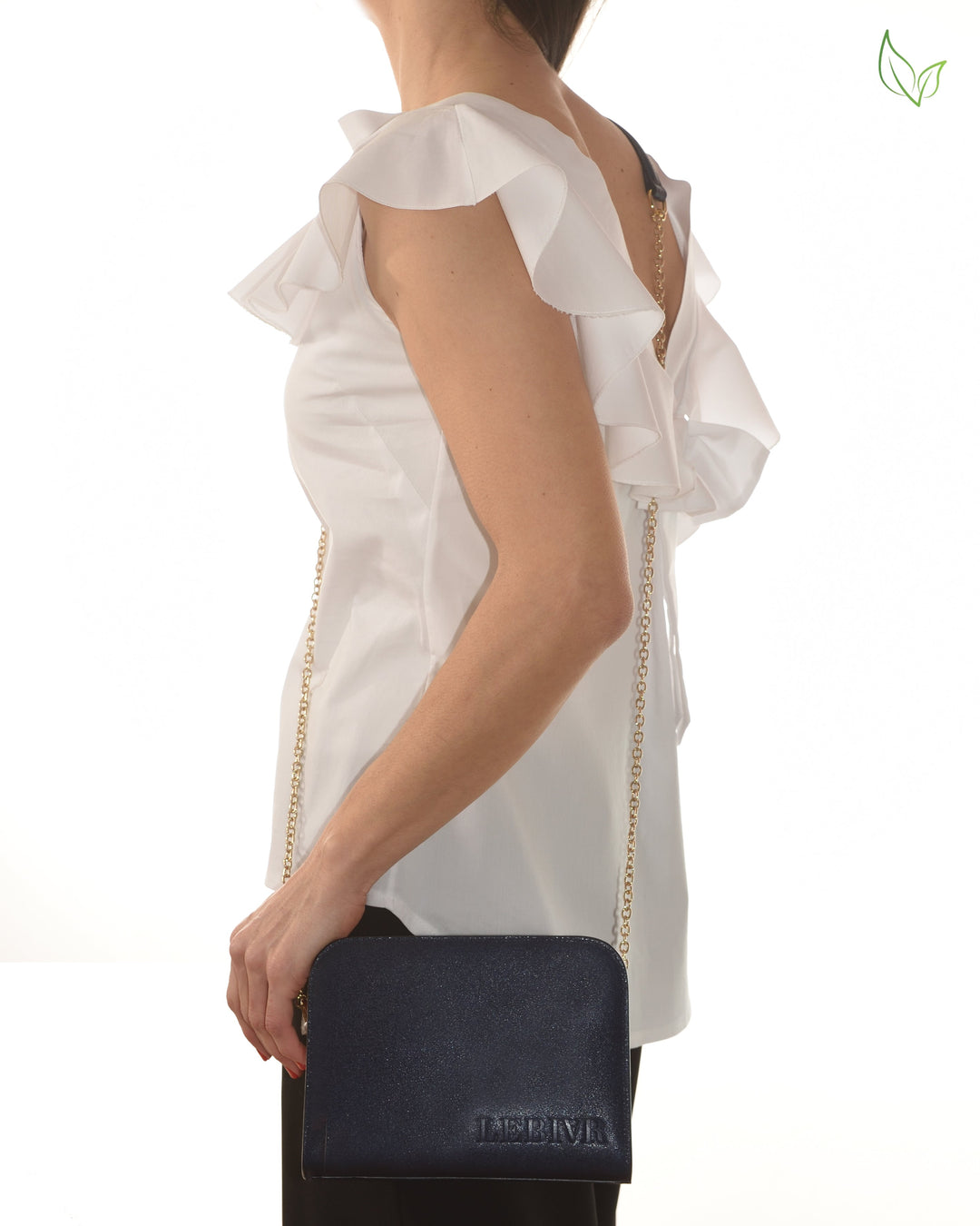 Woman wearing white ruffled blouse and holding a navy blue clutch bag with gold chain strap