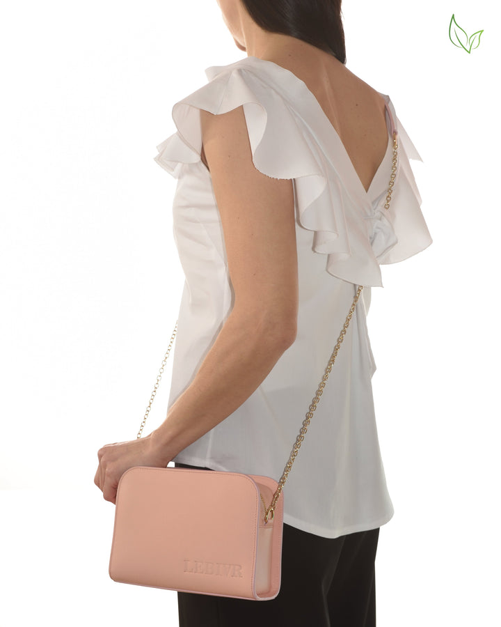 Woman wearing white ruffle sleeve top carrying a pink shoulder bag with gold chain strap