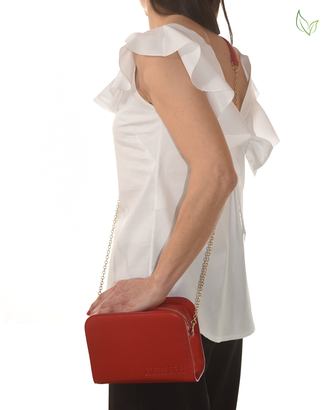 Woman holding a red leather handbag with gold chain strap wearing a white ruffled top