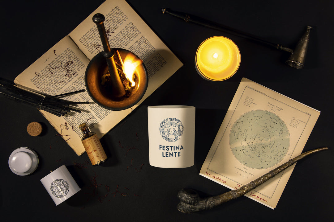 Vintage alchemy setup with open book, burning candle, celestial chart, and Festina Lente candle