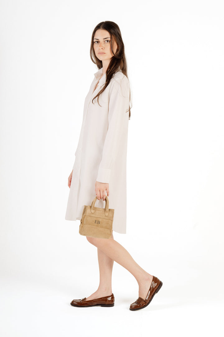 Woman modeling a white shirt dress with brown loafers and a beige handbag on a white background