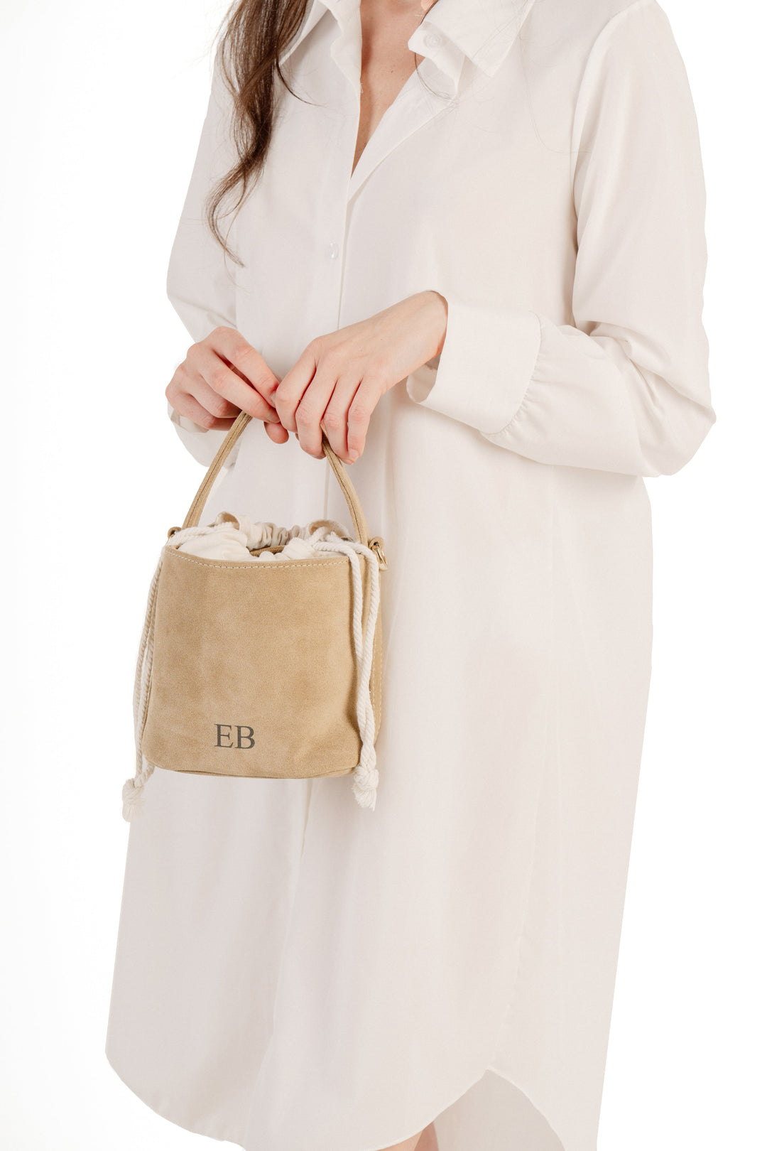 Woman in white dress holding a small beige suede handbag with rope handles