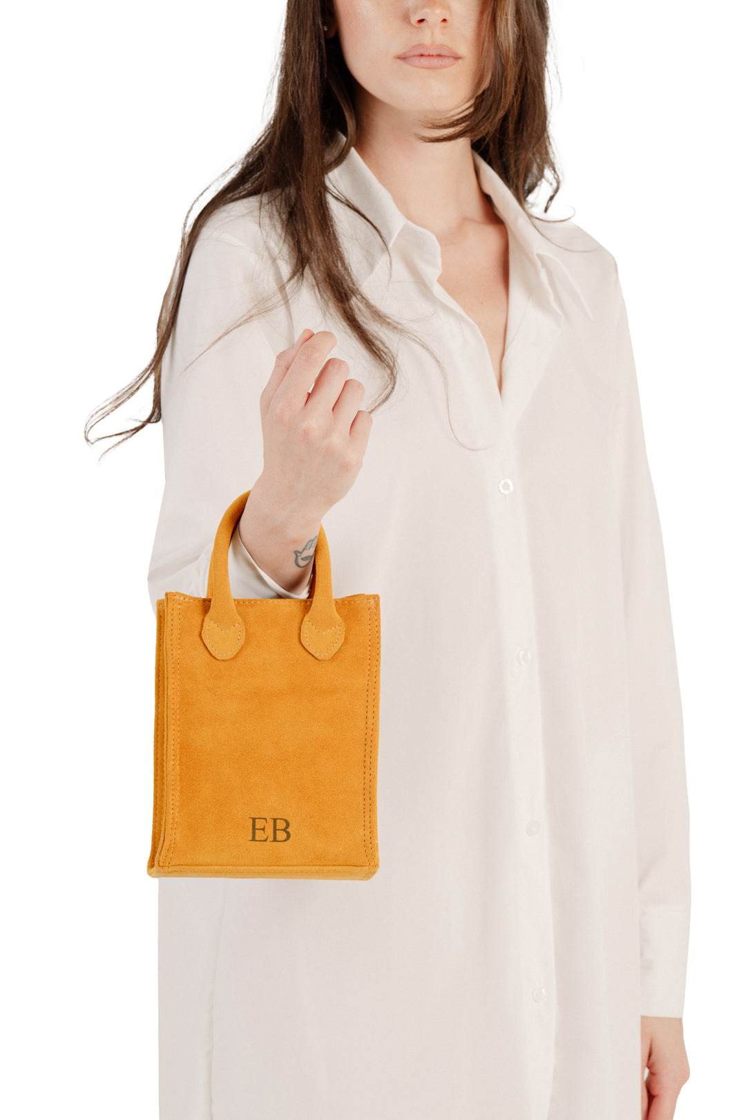 Woman holding a small yellow leather handbag with initials EB on it