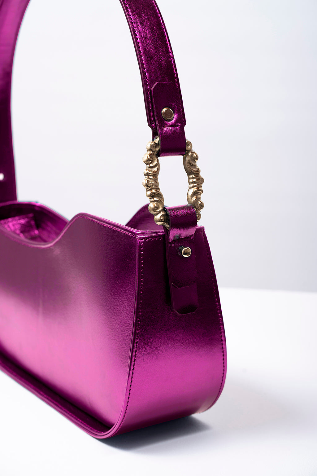 Shiny purple handbag with brass buckle detail on white background