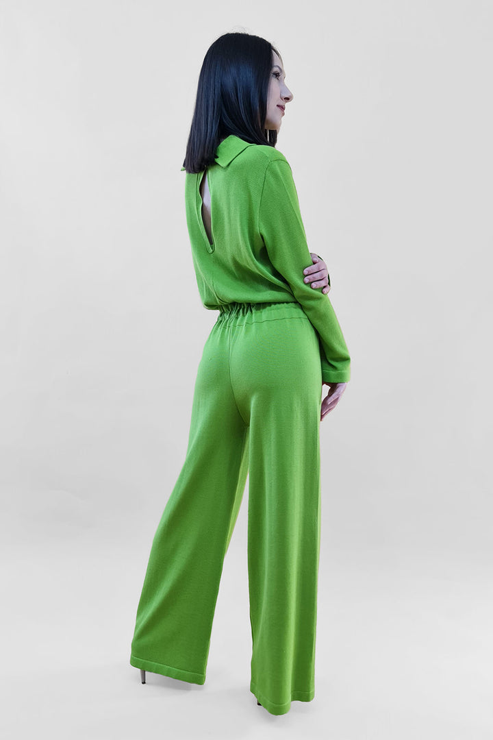 Woman in vibrant green, long-sleeve jumpsuit with open back posing against a solid background