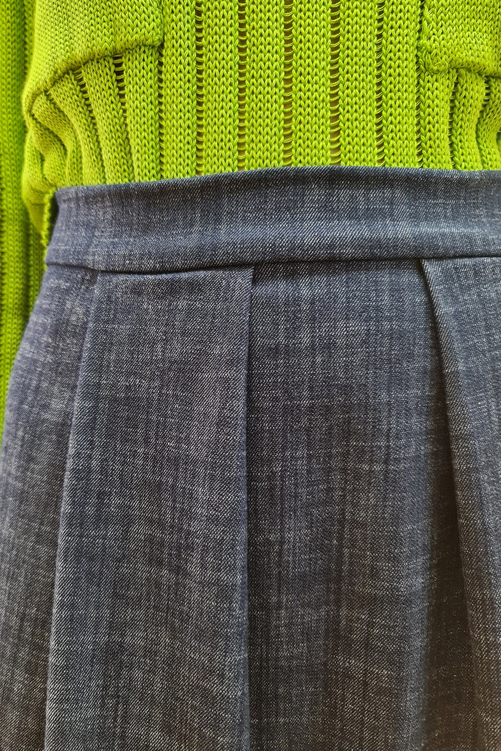 Close-up of a green knitted sweater paired with a gray pleated skirt