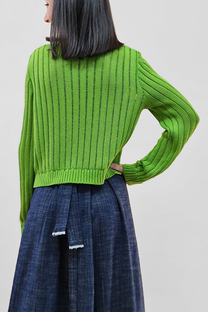 Woman wearing a green ribbed sweater and a denim skirt, viewed from the back