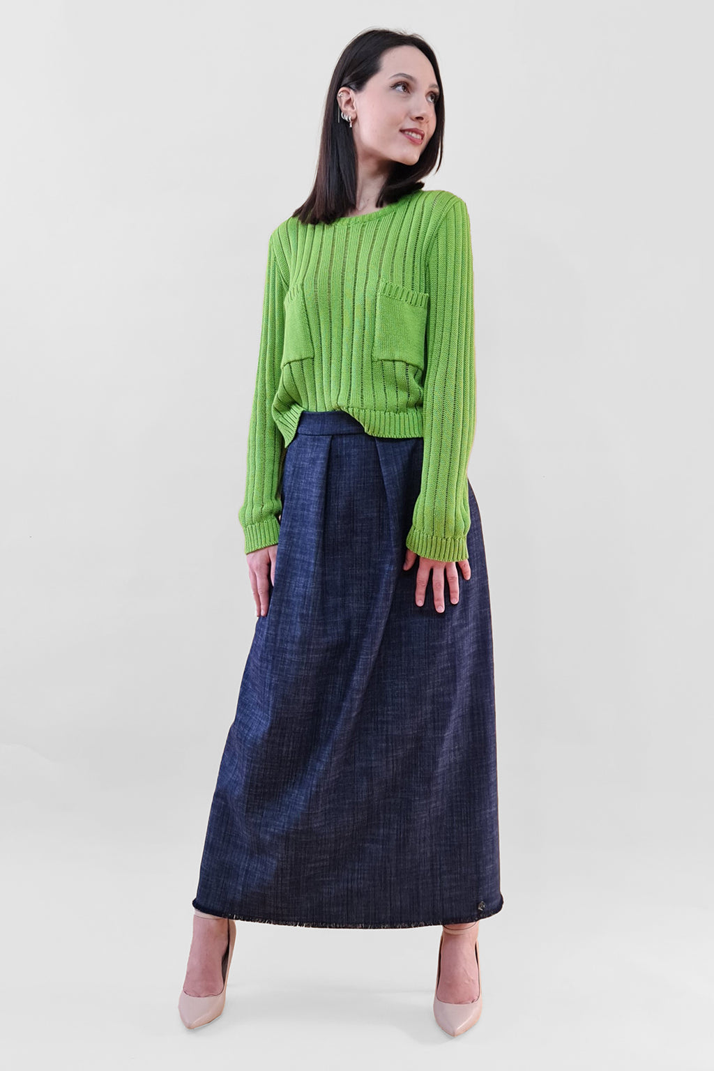 Woman wearing green sweater and long blue skirt standing on white background