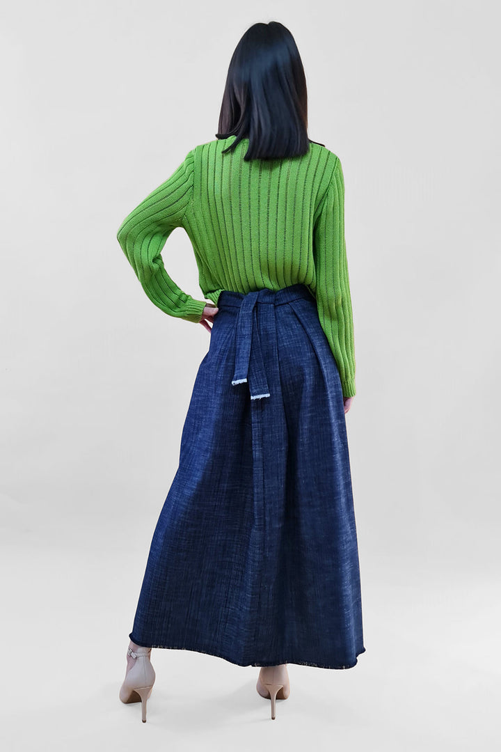 Person wearing a green ribbed sweater and blue wrap skirt, back view